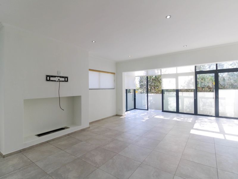 Spacious, light-filled living area featuring neutral tiled flooring, a built-in fireplace, and large aluminium sliding doors opening to an outdoor space.