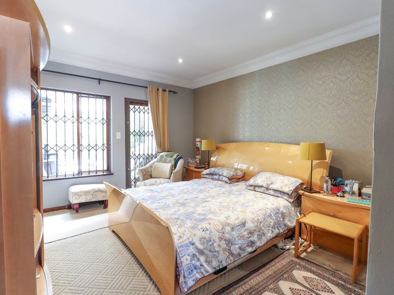 A well-proportioned bedroom featuring recessed downlights, decorative coving, and a feature wallpaper wall, with direct access to an outdoor area via a security gate.