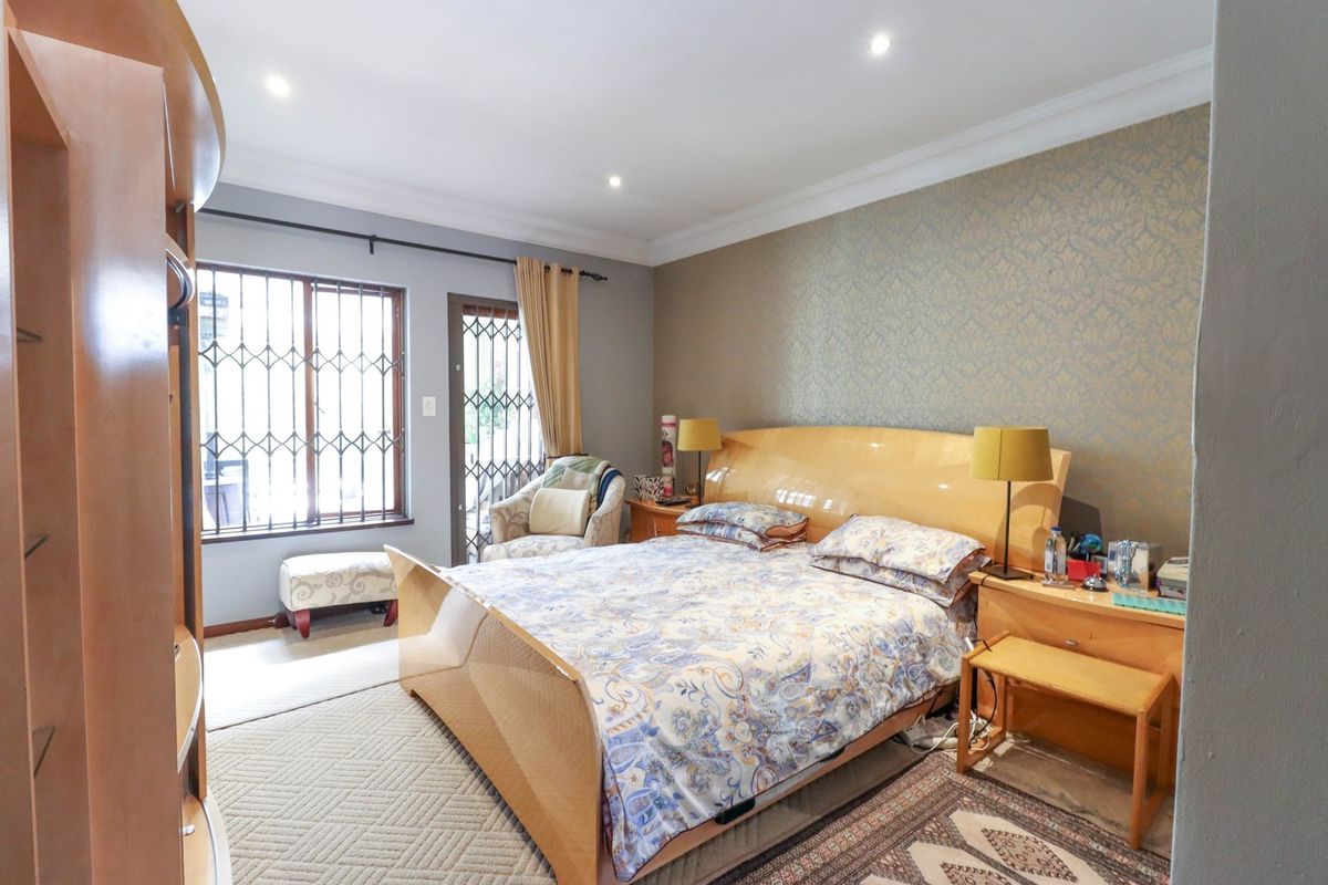 A well-proportioned bedroom featuring recessed downlights, decorative coving, and a feature wallpaper wall, with direct access to an outdoor area via a security gate.
