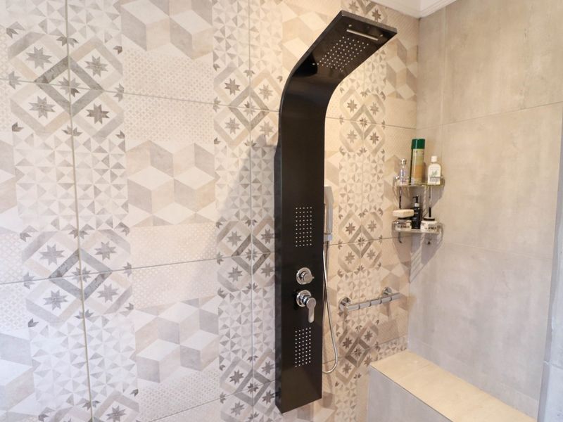 A modern bathroom shower area featuring a sleek black shower panel, patterned wall tiles, and a built-in tiled shower bench.