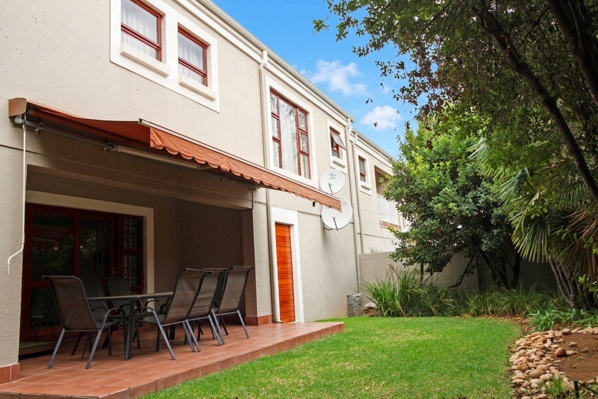 Rear view of the townhouse featuring a covered tiled patio with a retractable awning, overlooking a private landscaped garden and lawn.