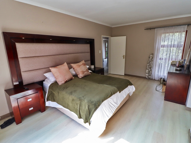 Spacious bedroom featuring light-toned laminate flooring, neutral wall finishes, and a large integrated headboard with built-in lighting.