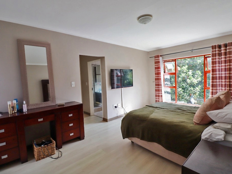 Spacious bedroom featuring light laminate flooring, large aluminium-framed windows, and direct access to an en-suite bathroom.