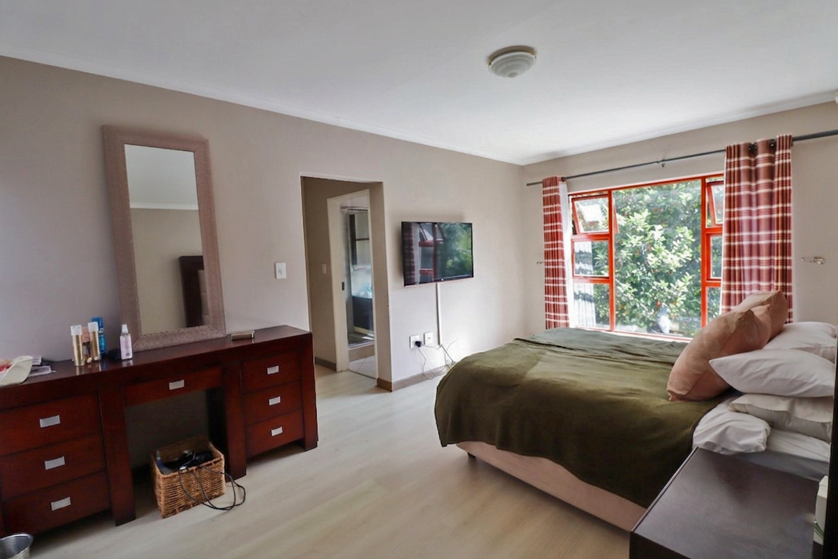 Spacious bedroom featuring light laminate flooring, large aluminium-framed windows, and direct access to an en-suite bathroom.