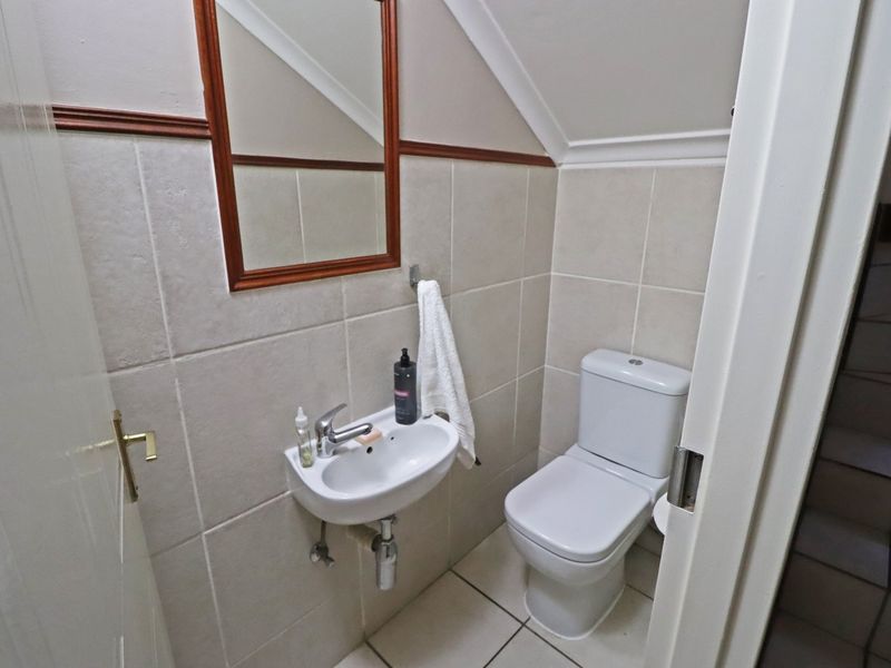A compact guest bathroom featuring a wall-mounted basin, toilet, and neutral wall tiling, situated under a staircase.