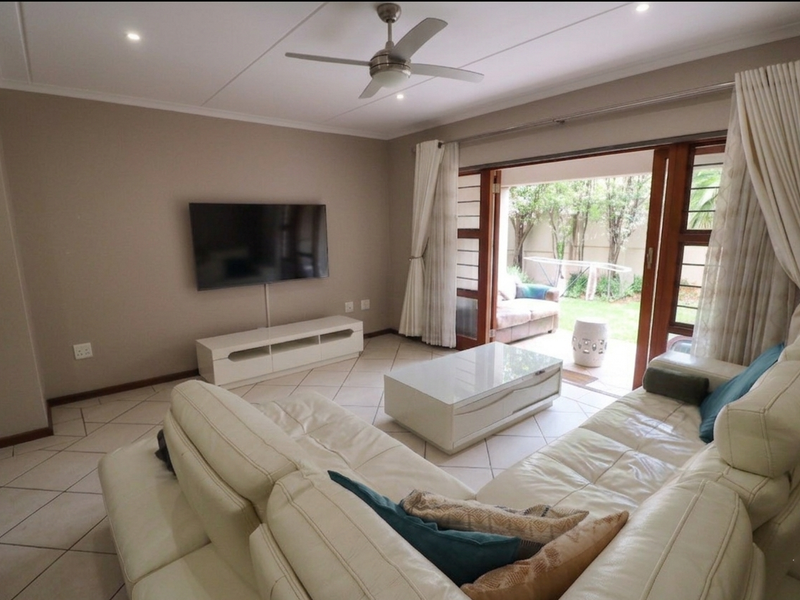 A bright living room featuring tiled flooring, a ceiling fan, and large sliding glass doors that provide direct access to the rear garden area.