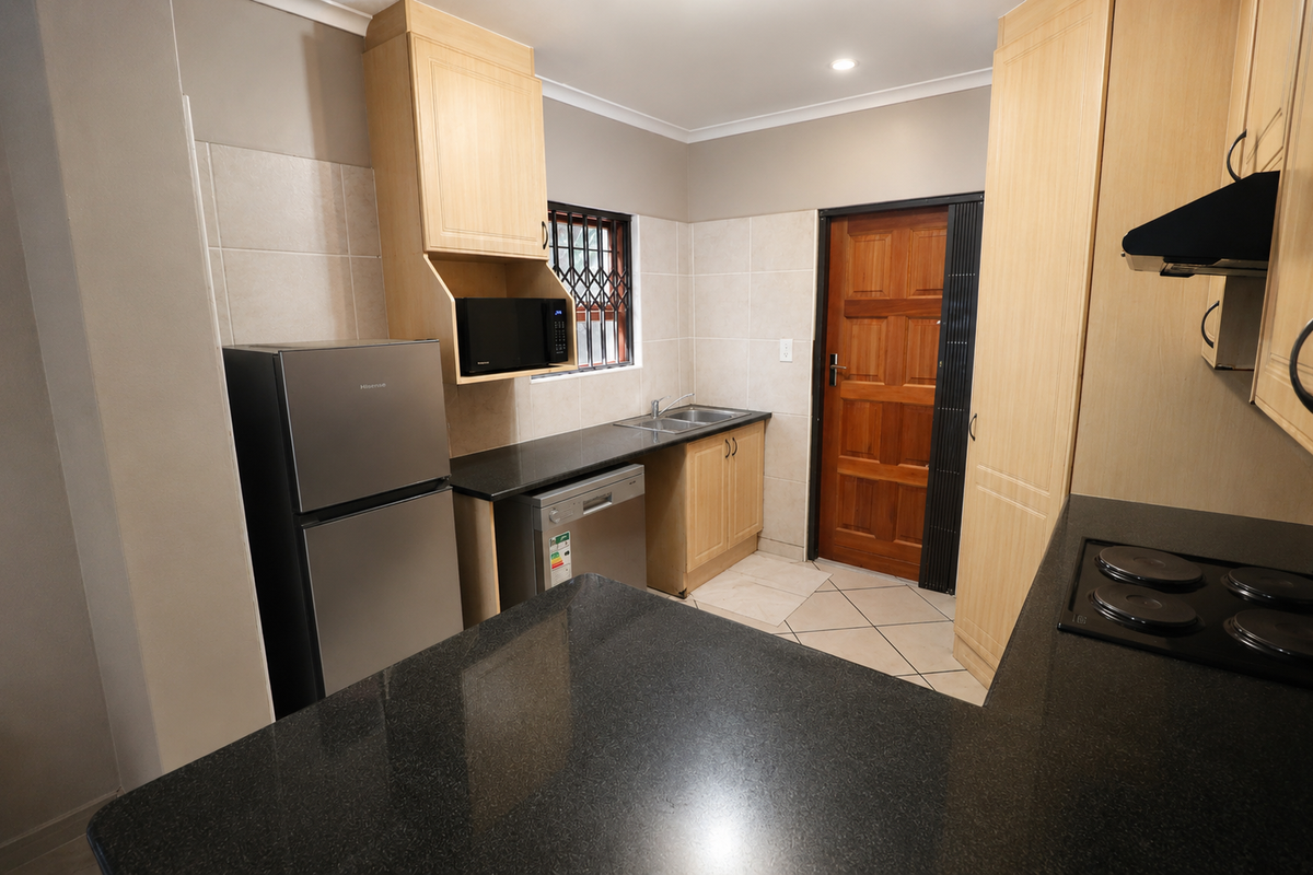 A functional kitchen featuring light wood cabinetry, dark granite countertops, a double sink, and an electric hob with an extractor fan.