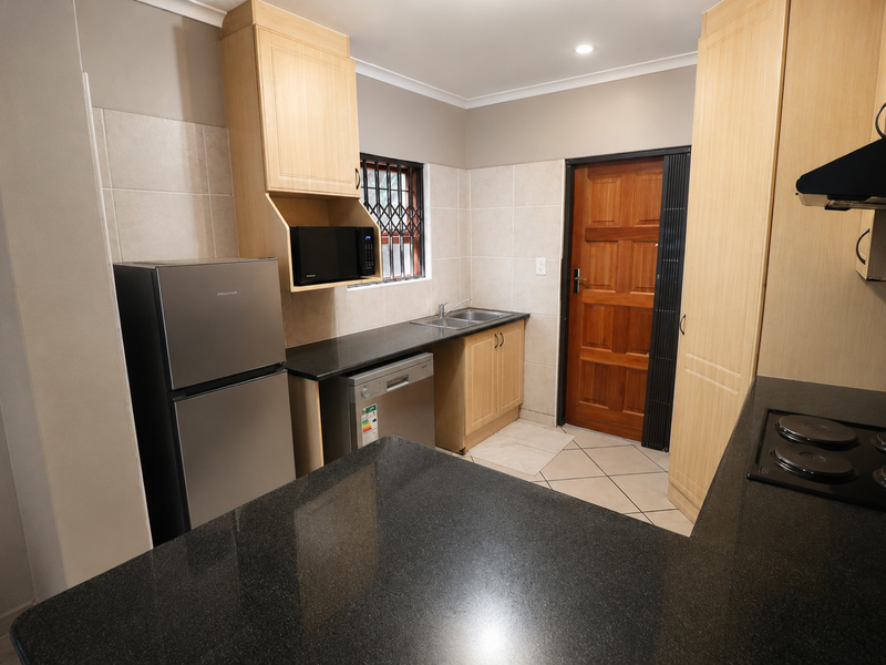 A functional kitchen featuring light wood cabinetry, dark granite countertops, a double sink, and an electric hob with an extractor fan.