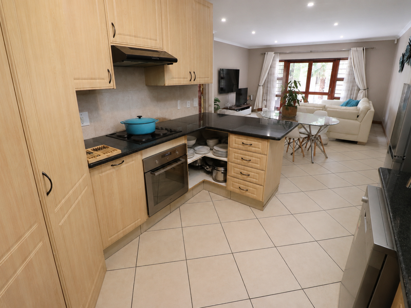 Open-plan kitchen and living area featuring light wood cabinetry, granite countertops, built-in appliances, and tiled flooring leading to a bright lounge space.