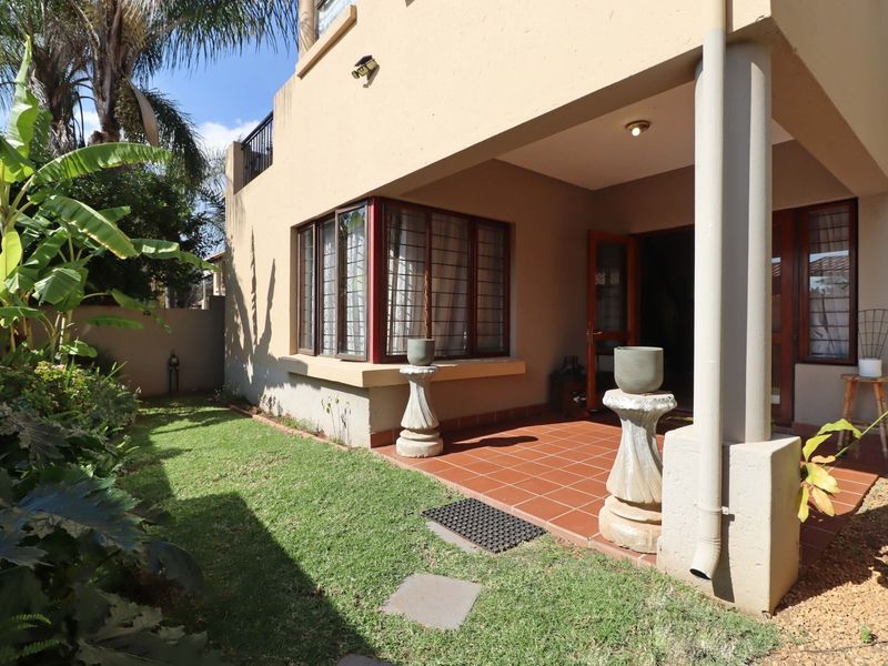 Rear view of the townhouse featuring a covered tiled patio, established garden, and security-fitted windows.