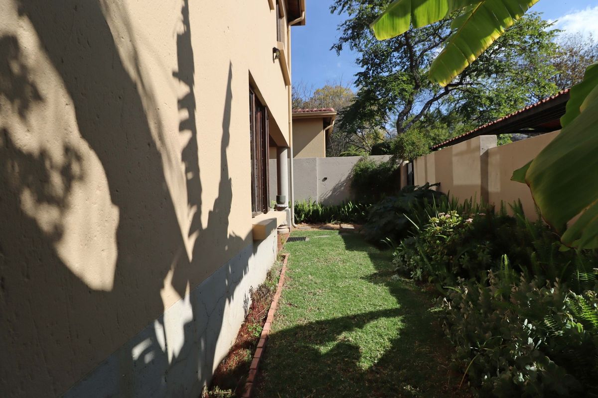 A side garden area featuring a lawn, brick edging, and a boundary wall along the side of the townhouse.