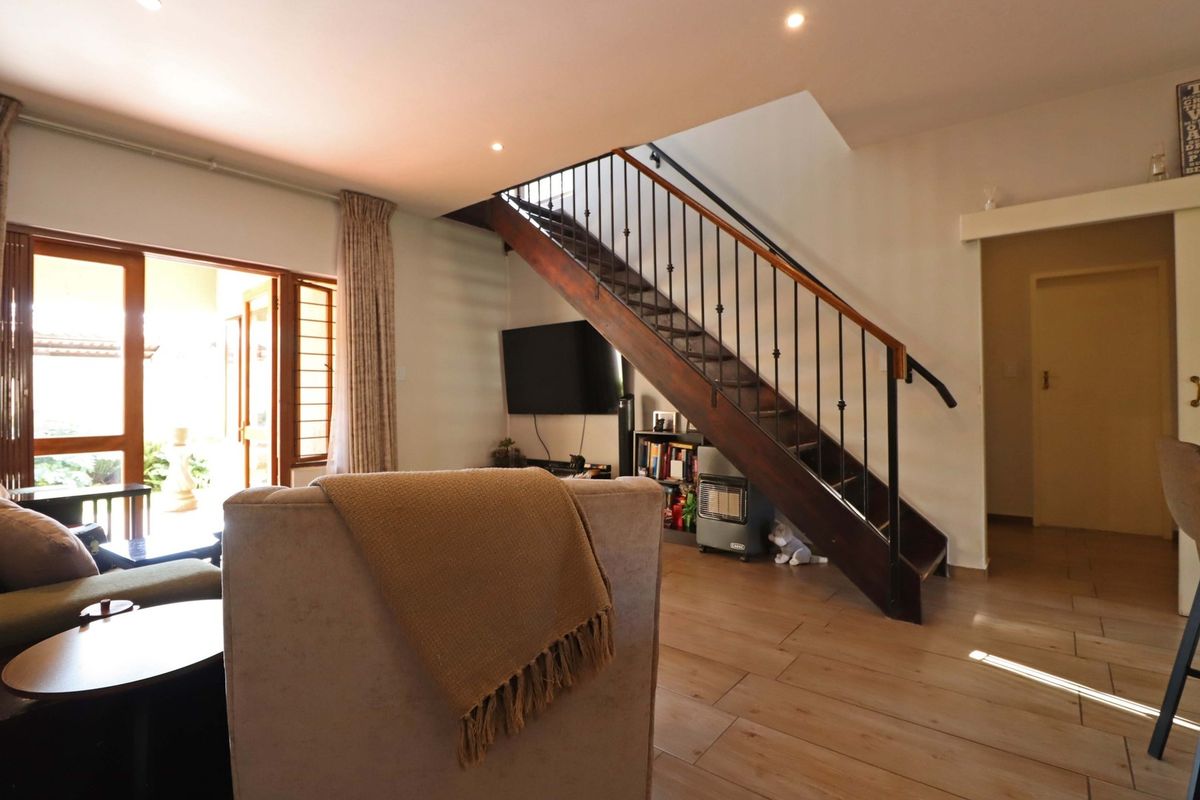 A bright living room featuring tiled flooring, recessed lighting, and a prominent wooden staircase with a wrought iron balustrade leading to the upper level.