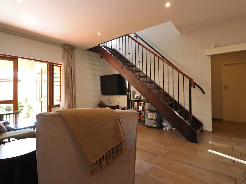 A bright living room featuring tiled flooring, recessed lighting, and a prominent wooden staircase with a wrought iron balustrade leading to the upper level.