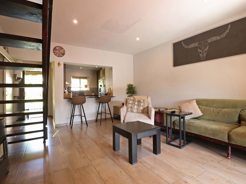 Open plan living area featuring tiled flooring, a breakfast bar connecting to the kitchen, and a staircase, with a visible ceiling stain.