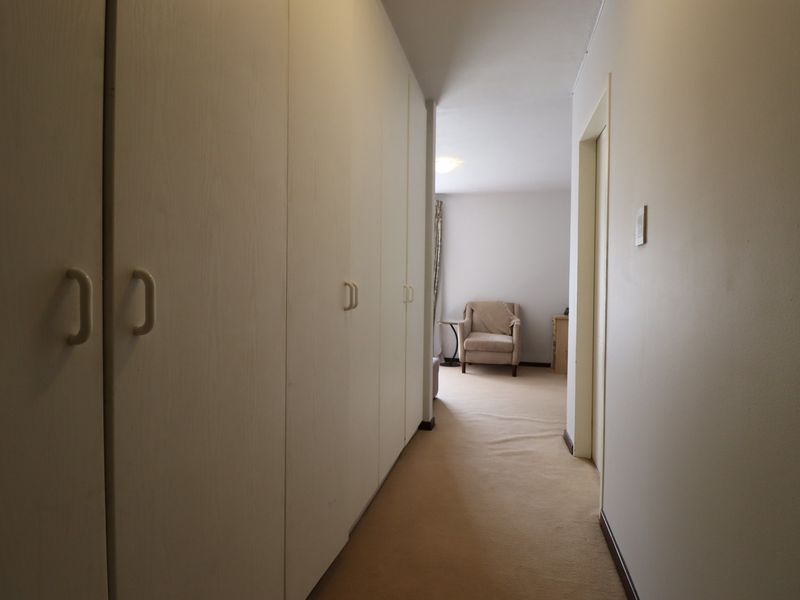 A functional hallway featuring extensive built-in cupboard storage and neutral carpeting, leading towards an adjacent room.