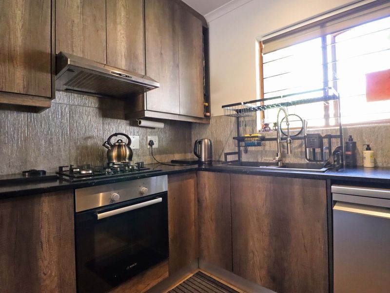 A functional kitchen featuring wood-look cabinetry, granite countertops, a gas hob, built-in oven, and a tiled backsplash with a window for natural light.