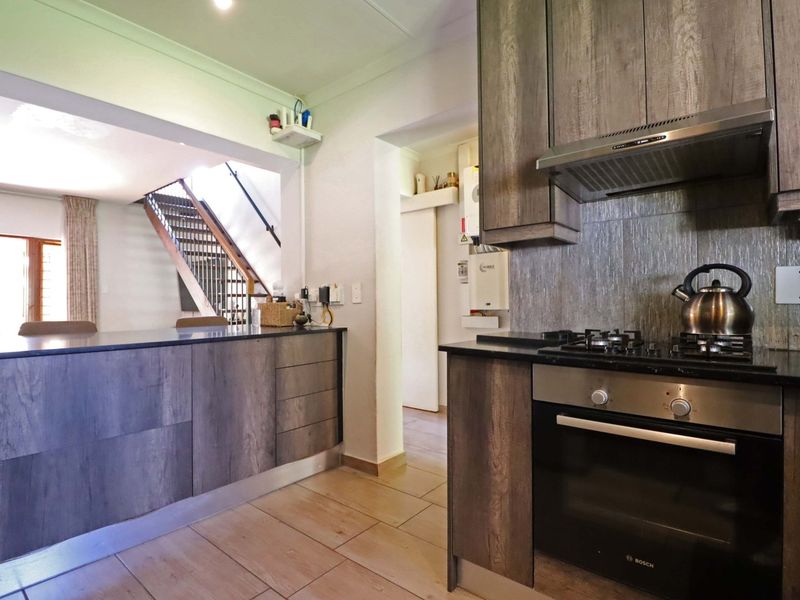 Modern kitchen featuring wood-look cabinetry, stone countertops, built-in gas hob and oven, with an open-plan layout leading to the staircase area.