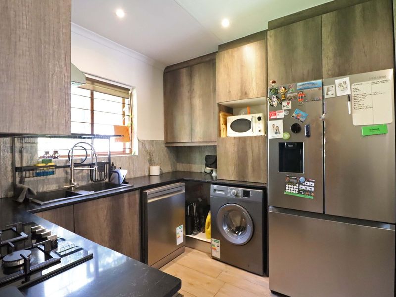 Modern kitchen featuring dark wood-look cabinetry, stone countertops, gas hob, extractor fan, and integrated appliances with a functional layout.