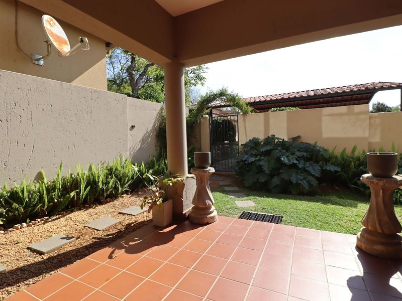 A covered patio area with tiled flooring, overlooking a private garden space with a boundary wall and gated access.