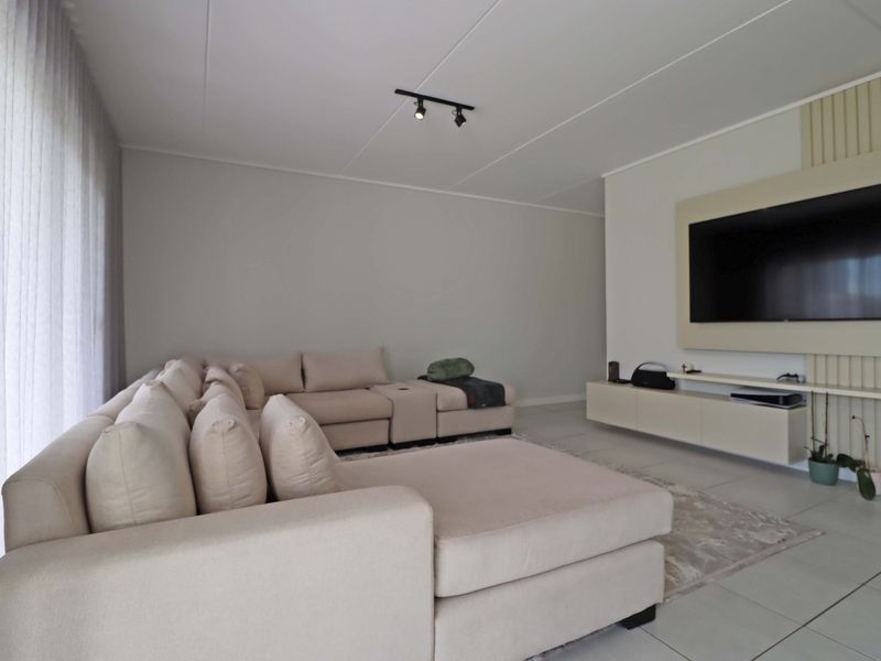 Modern living room featuring a built-in media console, decorative slatted wall paneling, track lighting, and neutral tiled flooring.