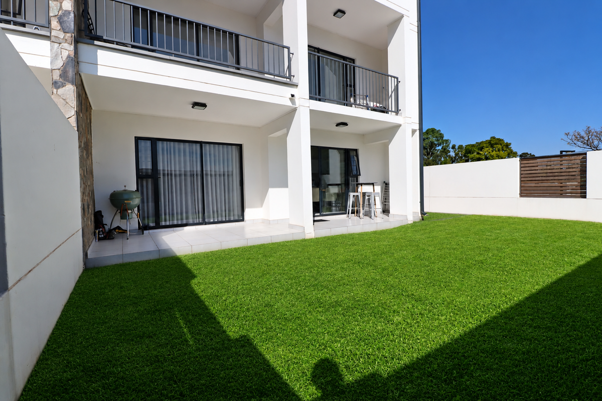 A well-maintained rear exterior featuring a tiled patio, artificial lawn, and a private garden area with modern balcony railings and sliding door access.