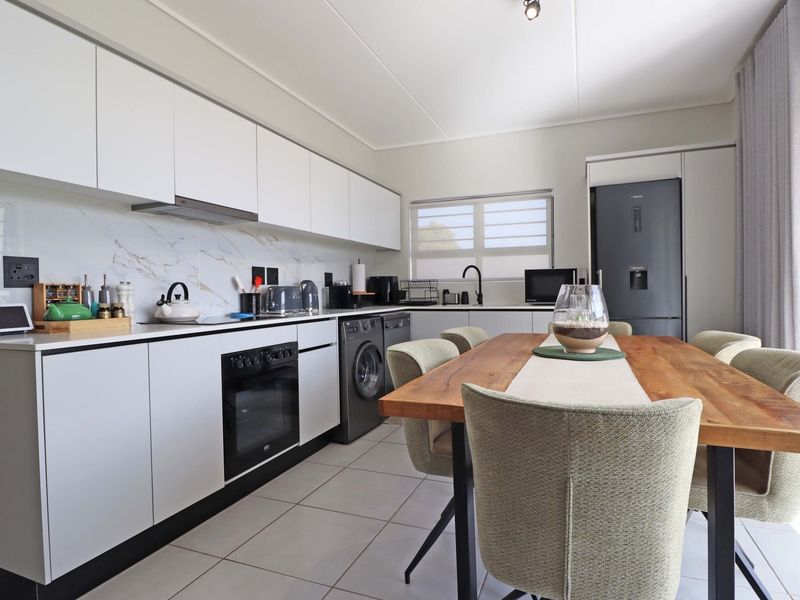 Modern open-plan kitchen featuring sleek white cabinetry, marble-look splashback, integrated appliances, and tiled flooring, seamlessly flowing into the dining area.