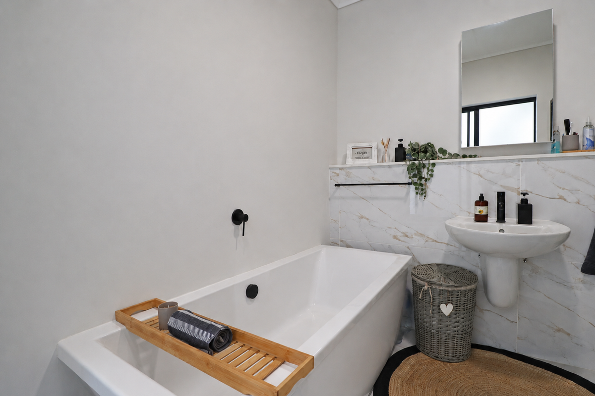 Modern bathroom featuring a sleek freestanding bathtub with wall-mounted fixtures, a pedestal sink, and elegant marble-look wall tiling.