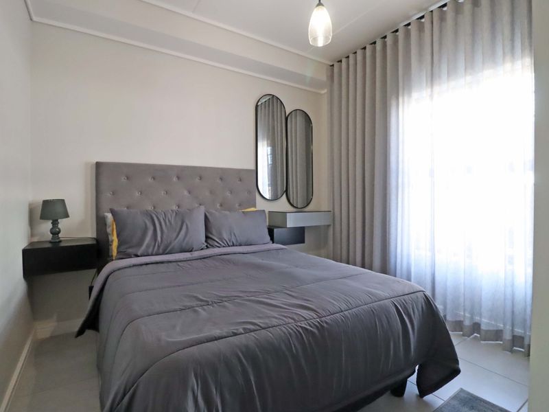 A well-maintained bedroom featuring neutral wall tones, tiled flooring, and a large window with floor-to-ceiling curtains.
