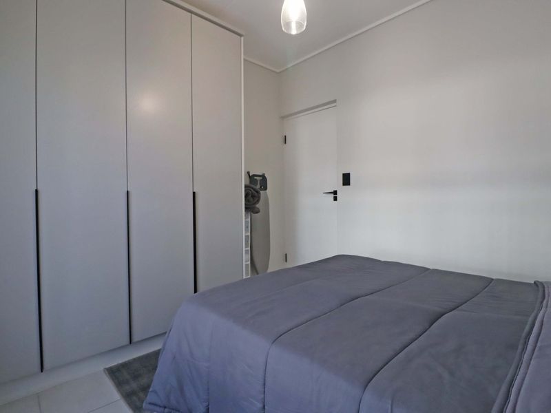 A clean and modern bedroom featuring floor-to-ceiling built-in wardrobes with sleek handles and neutral finishes.