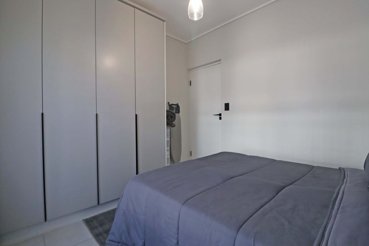 A clean and modern bedroom featuring floor-to-ceiling built-in wardrobes with sleek handles and neutral finishes.