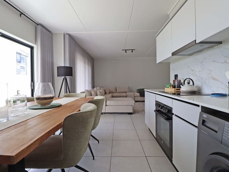 Modern open-plan living area featuring a sleek kitchen with marble-look splashback, built-in appliances, tiled floors, and seamless access to the outdoor space.