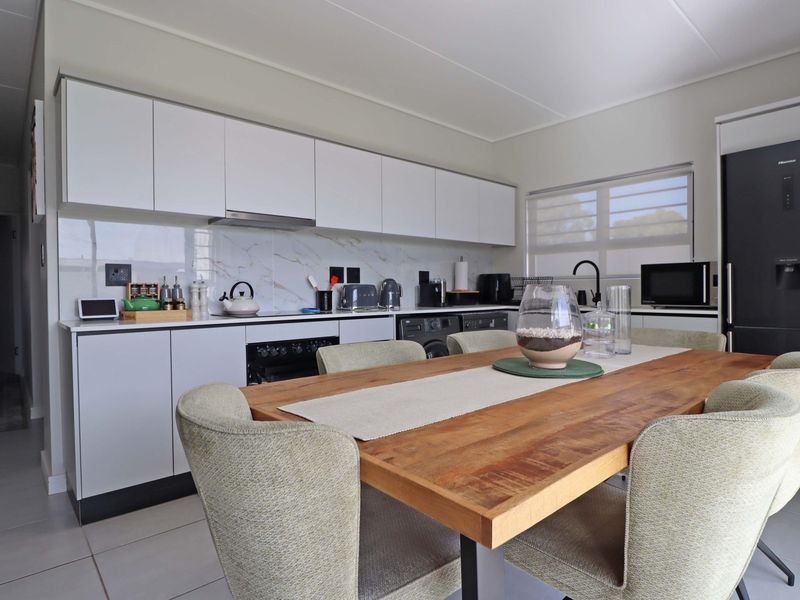 Modern open-plan kitchen featuring sleek white cabinetry, marble-look splashback, and integrated appliances, seamlessly flowing into the dining area with tiled flooring throughout.