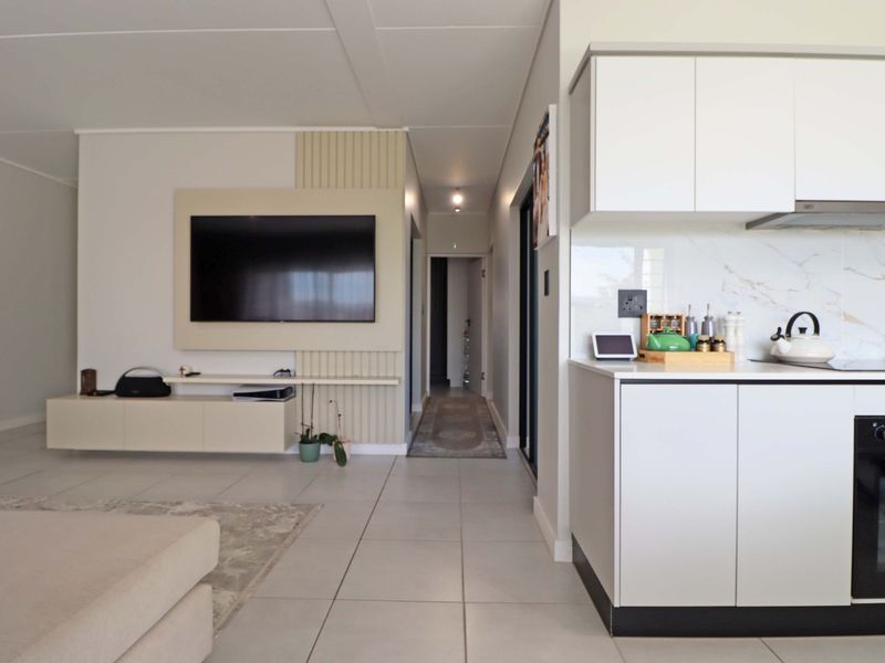 Modern open-plan living area featuring a sleek kitchen with integrated appliances and a contemporary built-in media wall, finished with neutral floor tiles.