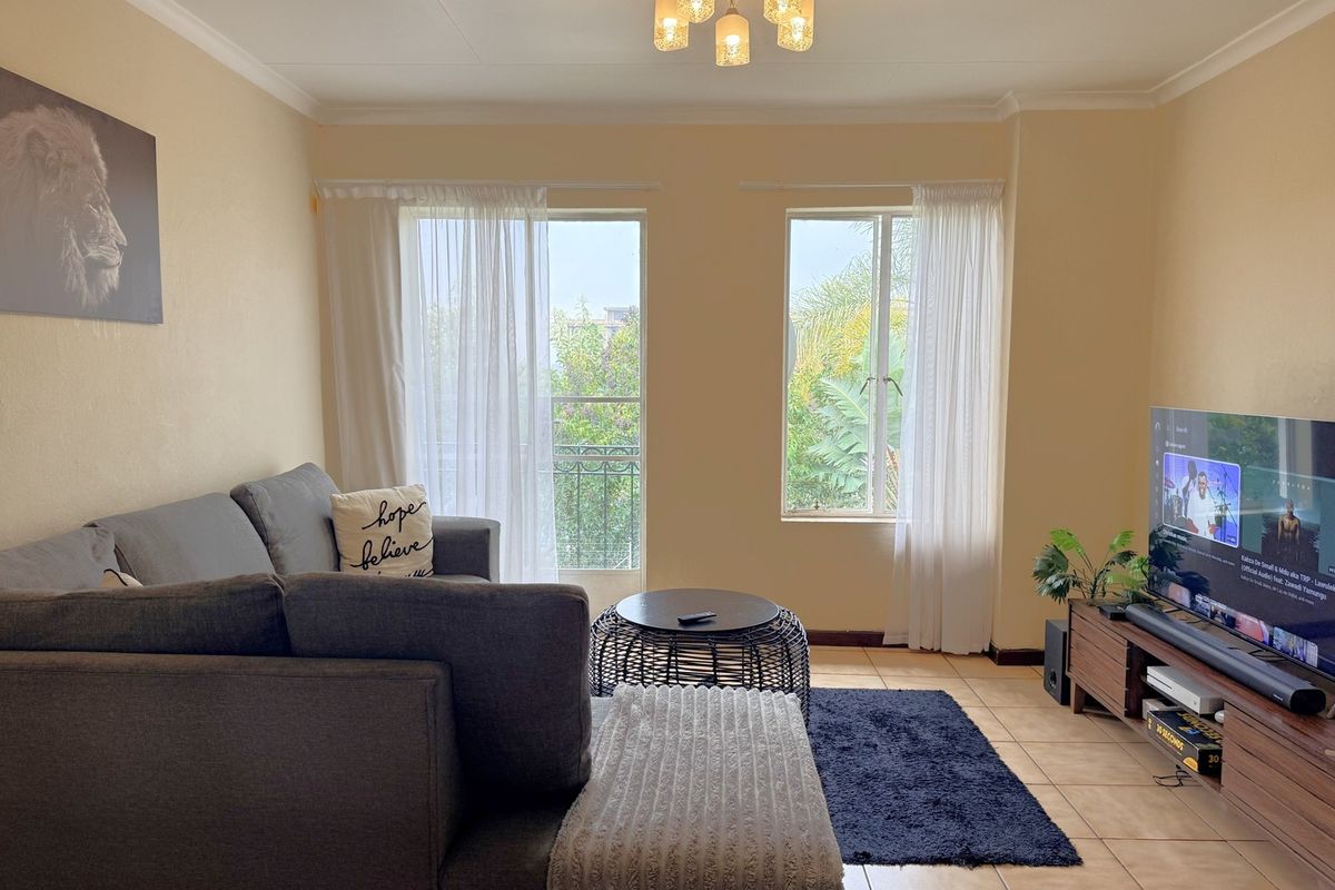 A comfortable living room featuring tiled flooring, coved ceilings, and natural light through a sliding glass door and window.