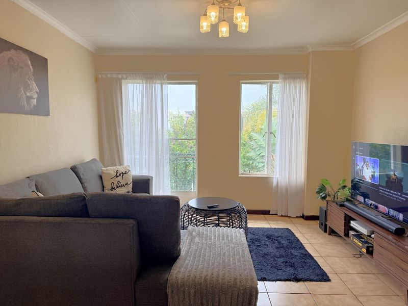 A comfortable living room featuring tiled flooring, coved ceilings, and natural light through a sliding glass door and window.