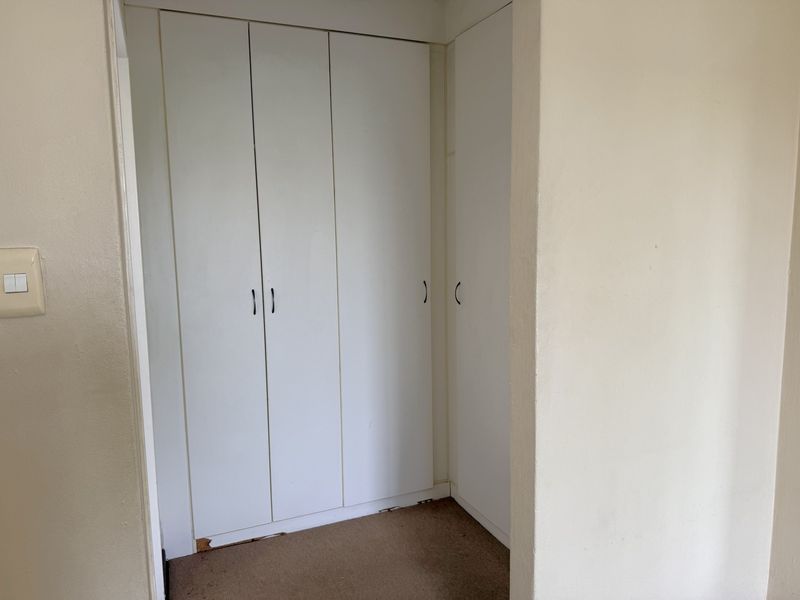 A bedroom featuring built-in cupboards with visible wear and damage to the base of the cabinetry.