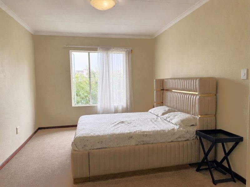 A neutrally painted bedroom featuring carpeted flooring, a coved ceiling, and a window providing natural light.