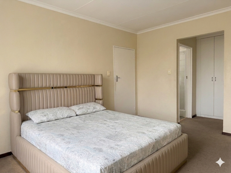 A spacious bedroom featuring neutral walls, carpeted flooring, and built-in cupboards, with direct access to an adjoining bathroom area.