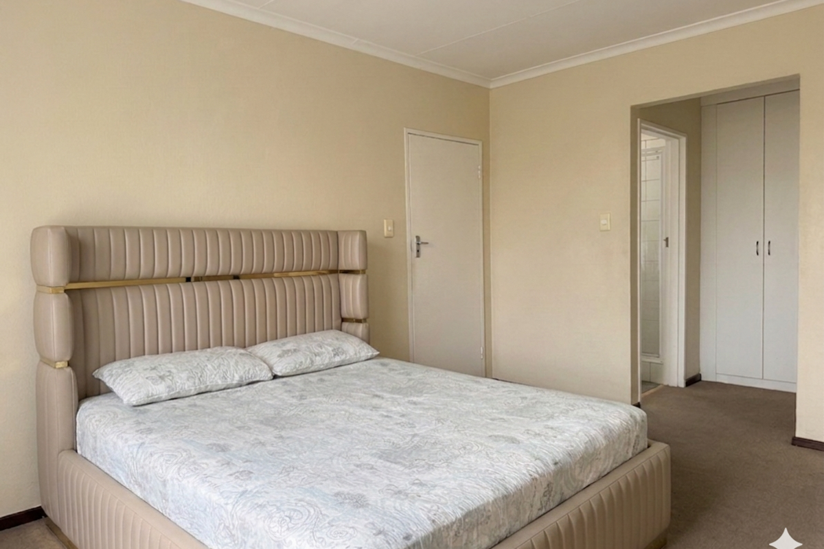 A spacious bedroom featuring neutral walls, carpeted flooring, and built-in cupboards, with direct access to an adjoining bathroom area.