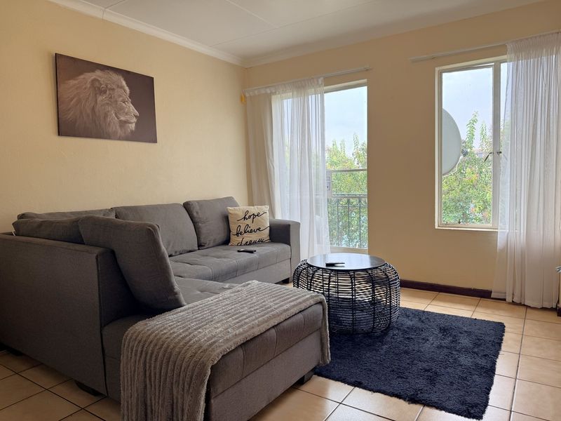 A comfortable living room featuring tiled flooring, a sliding glass door leading to a balcony, and large windows providing natural light.