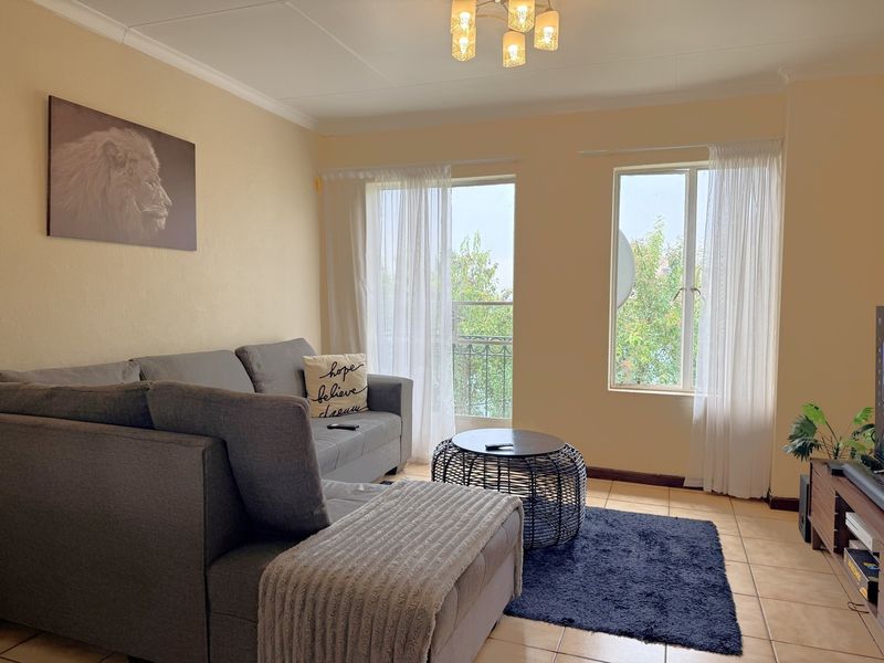 A comfortable living room featuring tiled flooring, natural light from large windows, and direct access to a balcony area.