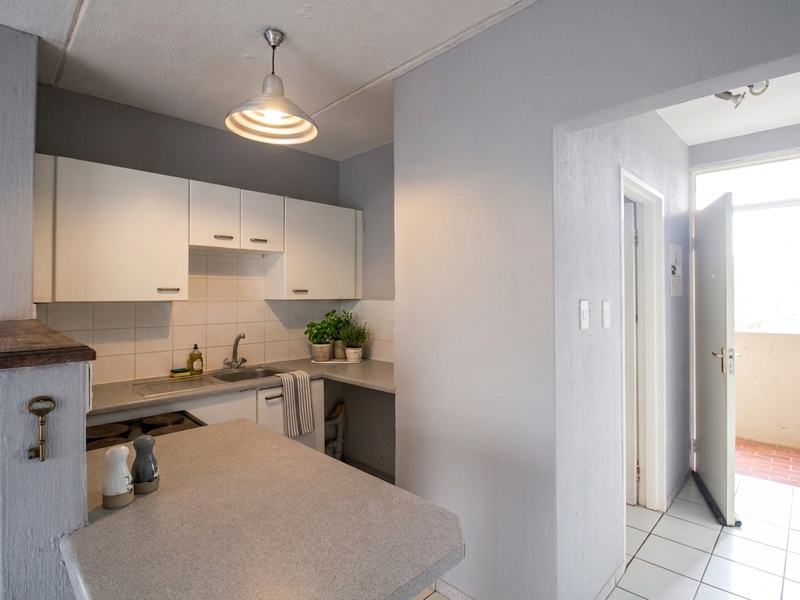 Compact kitchen featuring built-in cabinetry, laminate countertops, a stainless steel sink, and an electric stove, with direct access to an outdoor balcony area.