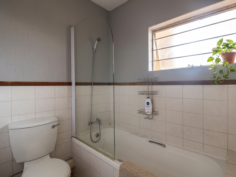 A functional bathroom featuring a bathtub with a glass shower screen, a toilet, and tiled wall finishes with a window for natural light.