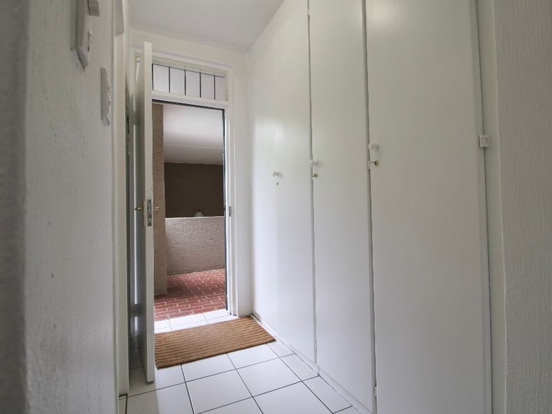 A bright hallway featuring white built-in cupboards and tiled flooring, leading to an exterior entrance area.
