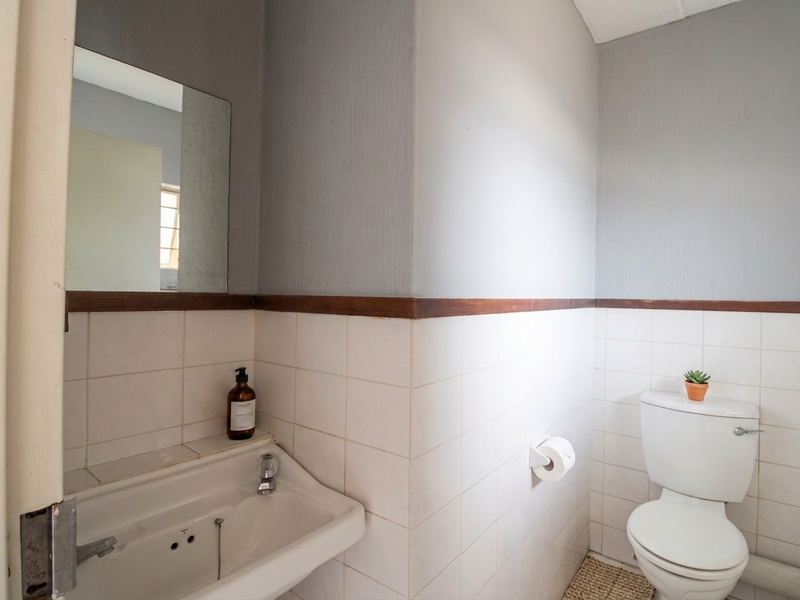 A functional bathroom featuring a wall-mounted basin, toilet, and tiled splashback with timber detailing, offering a clean and simple layout.
