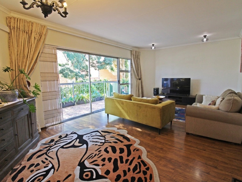 Spacious living room featuring laminate flooring, air conditioning, and large sliding glass doors providing direct access to a private balcony.