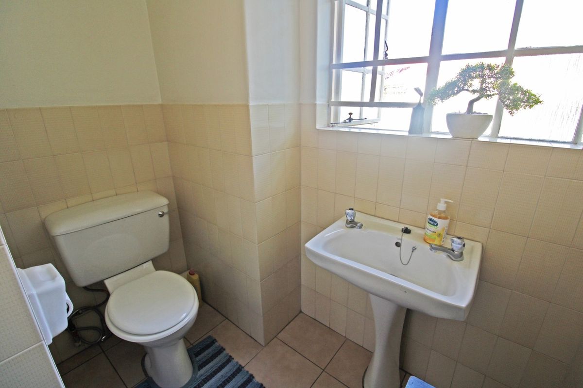 A functional bathroom featuring a pedestal basin, toilet, and neutral wall and floor tiling with natural light from a casement window.