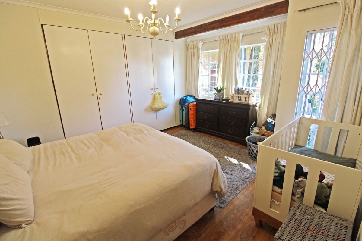 A bedroom featuring built-in cupboards, laminate flooring, and a decorative timber ceiling beam, with natural light entering through the windows.