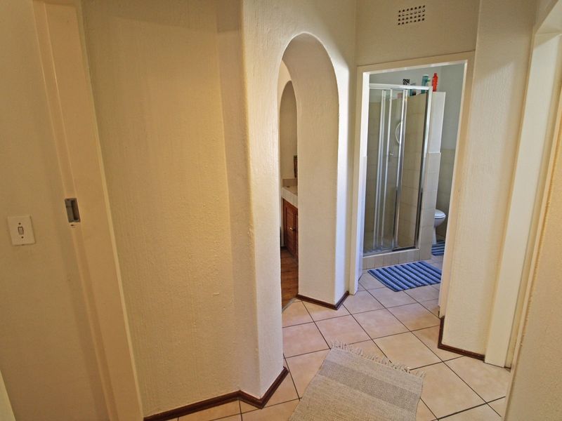 A tiled hallway featuring an arched architectural detail leading towards a bathroom with a shower enclosure.