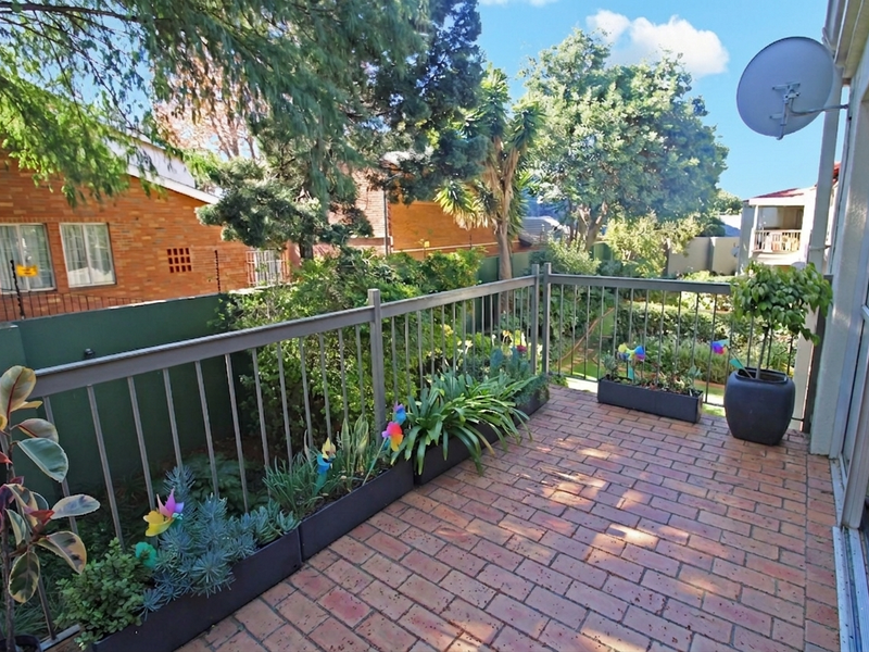 A private balcony featuring brick paving and a metal balustrade, overlooking a lush garden area.